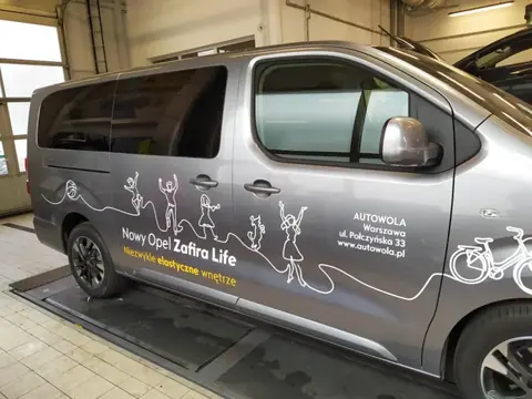 Opel Zafira Life oklejony grafiką z rysunkiem rodziny i adresem salonu Autowola