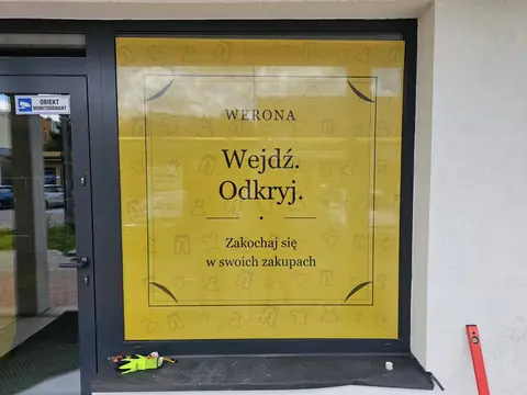 Drzwi sklepu Werona oklejone żółtą grafiką z hasłem Wejdź. Odkryj.
