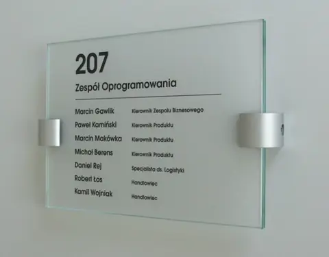Szklana tabliczka na drzwi biura z numerem pokoju i nazwiskami zespołu